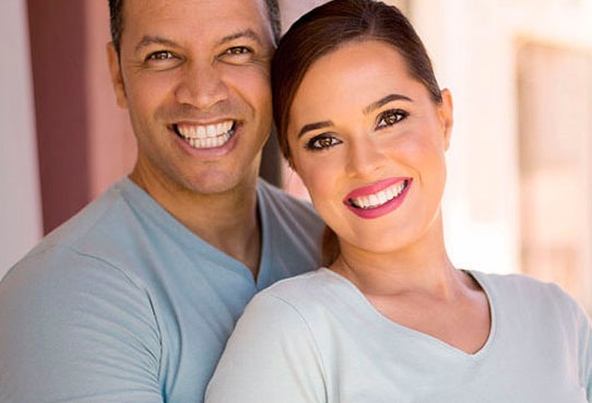Smiling couple with matching light blue shirts pose closely together outdoors, radiating joy and warmth, ideal for promoting togetherness and relationships.